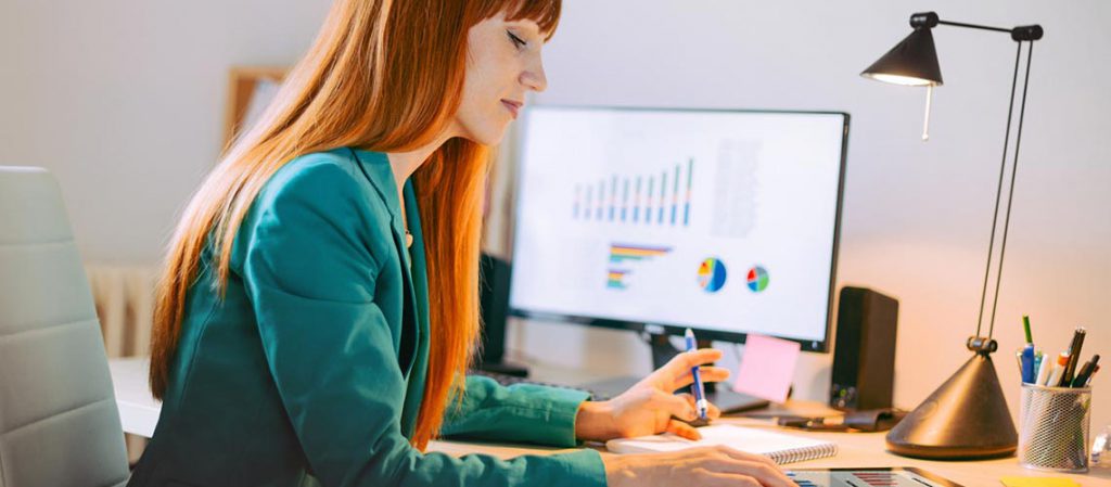 Mujer revisando gráficos financieros en una pantalla de ordenador en su oficina, analizando datos relacionados con fondos de inversión