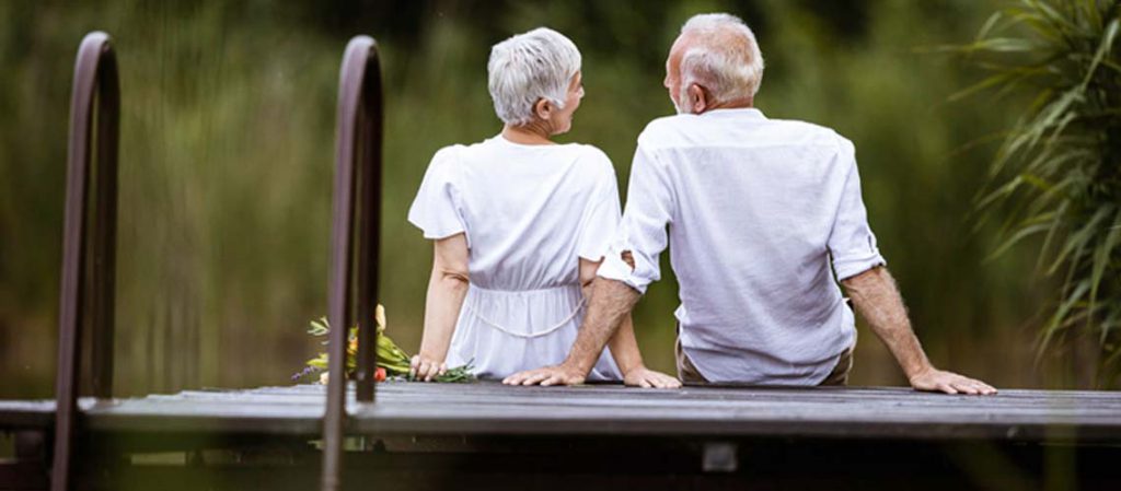 Pareja de adultos mayores sentados en un muelle, disfrutando de un momento juntos al aire libre, representando la tranquilidad que puede ofrecer un buen plan de pensiones