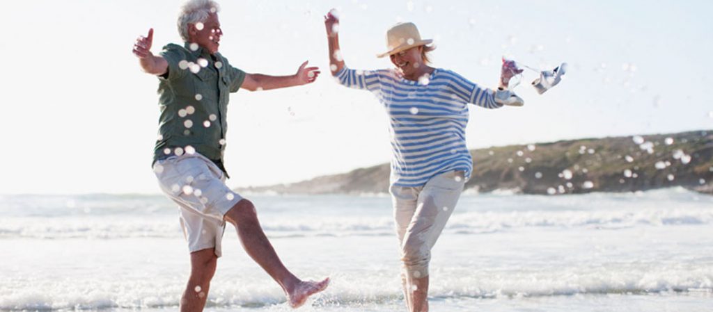 Pareja de adultos mayores disfrutando de un día en la playa, jugando con el agua, representando las ventajas de la jubilación parcial