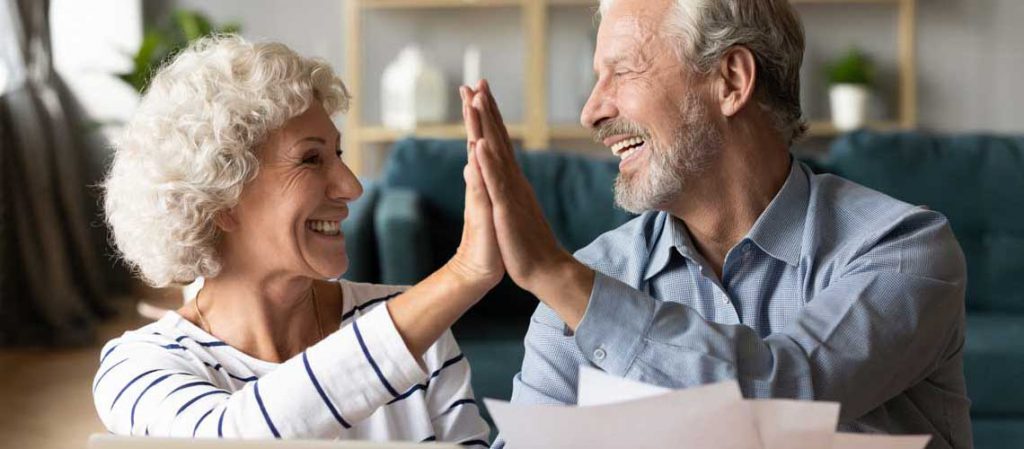 Pareja de adultos mayores celebrando con un gesto de choque de manos en casa, reflejando la satisfacción y seguridad que brindan un plan de pensiones o fondos de inversión en la jubilación